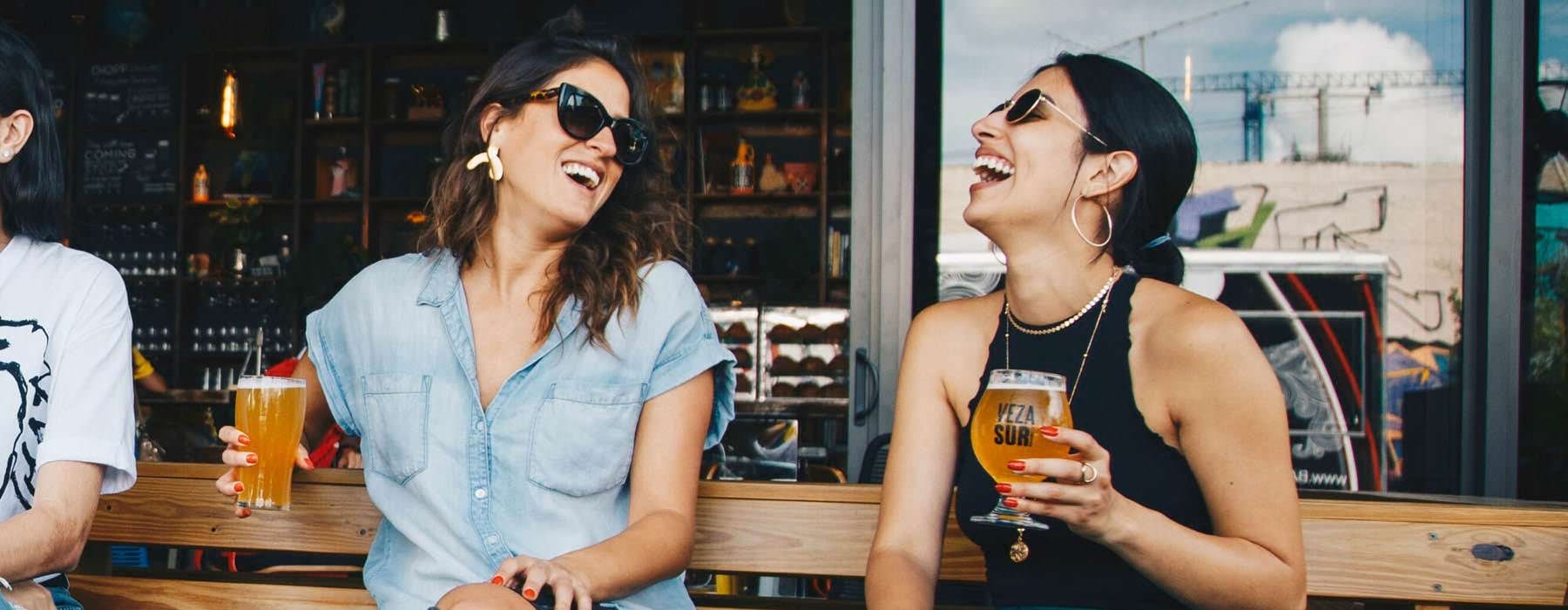 women with beers laugh outside pub